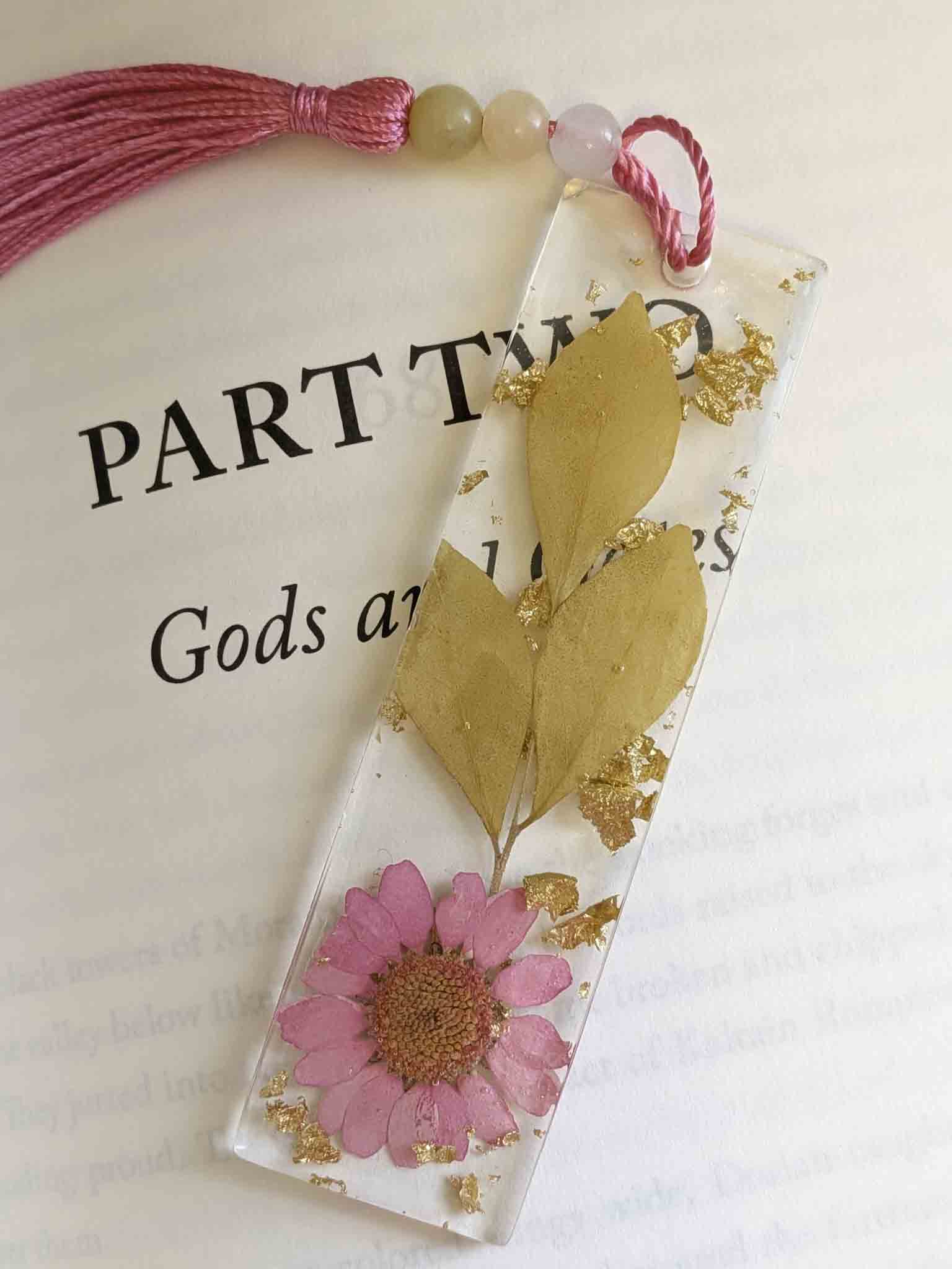 Decorative bookmark with pink flower and gold leaves on a book page.