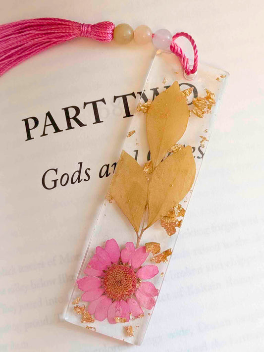 Decorative bookmark with pink flower and gold leaves on a book page.